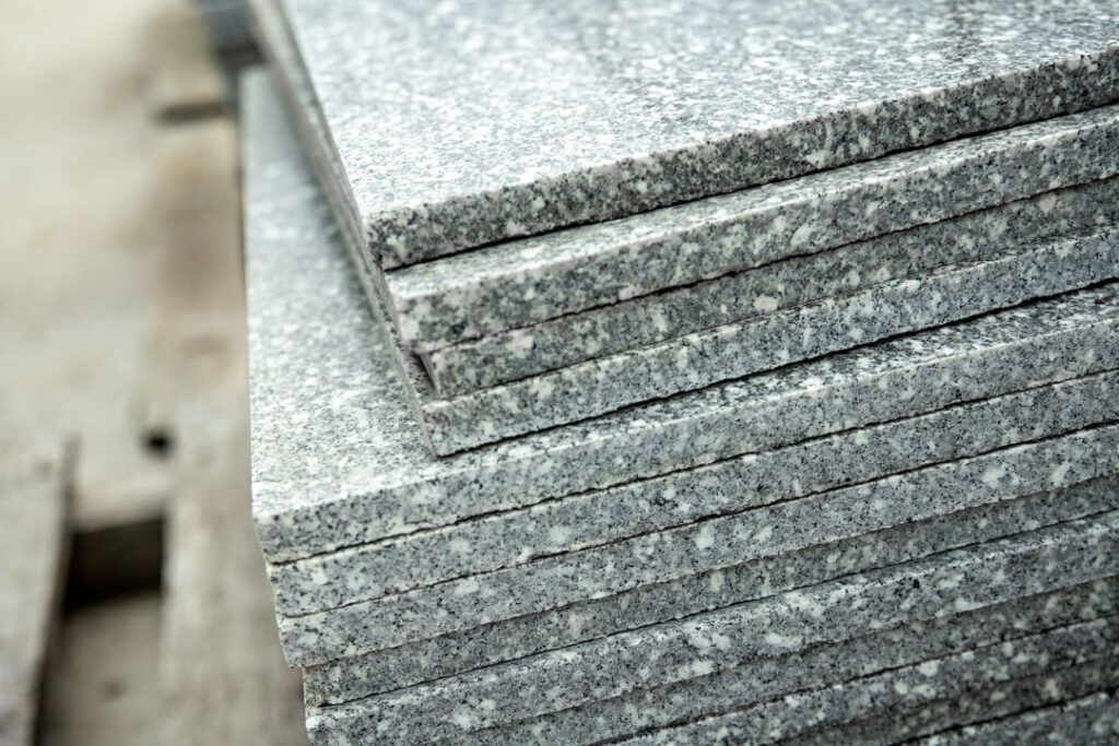 Pilha de placas de granito cinza claro, com superf&iacute;cie polida e bordas retas, empilhadas em ambiente de obra.