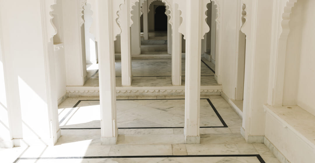 Interior de construção clara com piso de quartzito Taj Mahal e colunas com arcos ornamentados em estilo indiano.