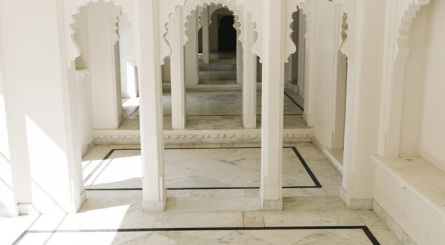 Interior de construção clara com piso de quartzito Taj Mahal e colunas com arcos ornamentados em estilo indiano.