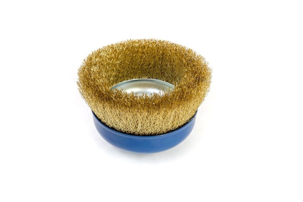 Imagem de uma das escovas de acabamento fosco, com cerdas met&aacute;licas douradas e base azul, utilizada para polimento e limpeza de superf&iacute;cies.
