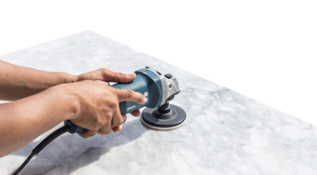 Profissional utilizando uma politriz elétrica para polir a superfície de uma pedra de mármore.