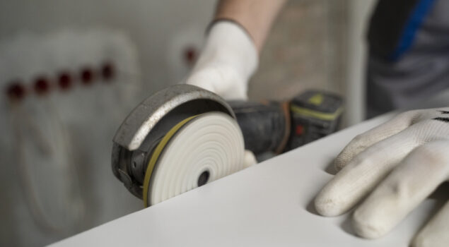 Profissional utilizando uma lixadeira elétrica para polir a borda de uma superfície de mármore, representando o uso de lixas e discos de corte Cobral em processos de acabamento.